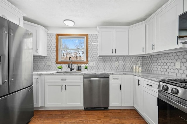 kitchen with a sink, white cabinetry, appliances with stainless steel finishes, light stone countertops, and dark wood finished floors