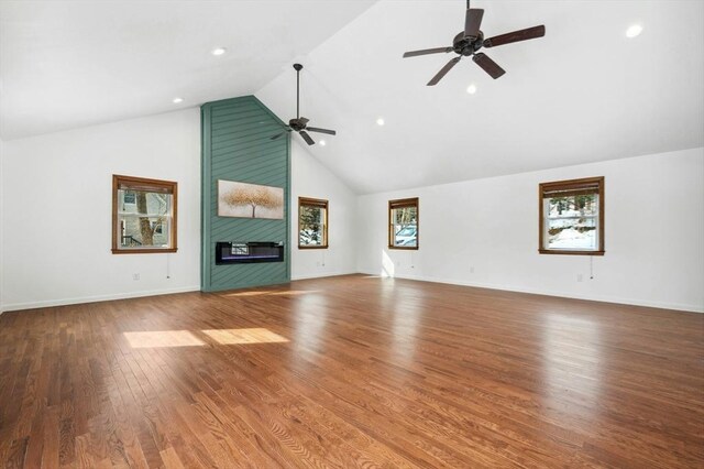 unfurnished living room with ceiling fan, high vaulted ceiling, a large fireplace, wood finished floors, and baseboards