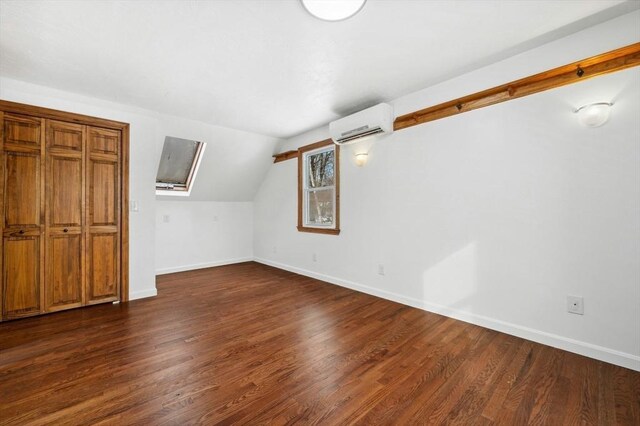 additional living space with dark wood-type flooring, a wall mounted air conditioner, vaulted ceiling, and baseboards