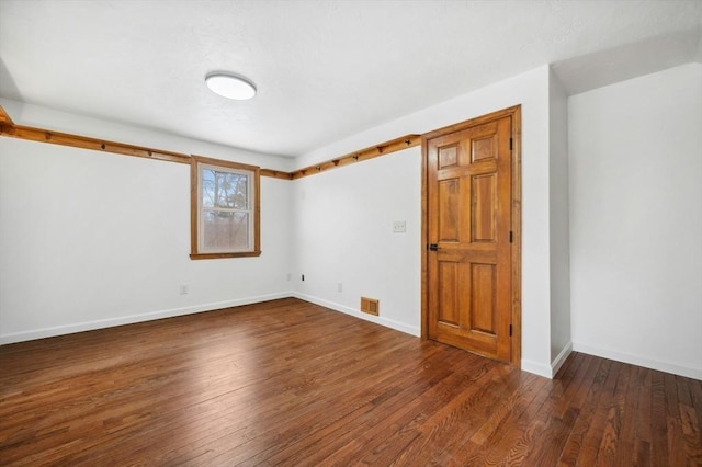 empty room with dark wood-style floors, visible vents, and baseboards