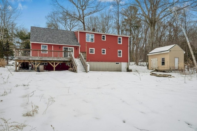 snow covered rear of property featuring a chimney, stairs, a deck, an outdoor structure, and a shed