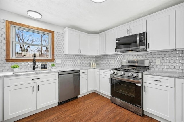 kitchen with light stone countertops, white cabinetry, stainless steel appliances, and a sink