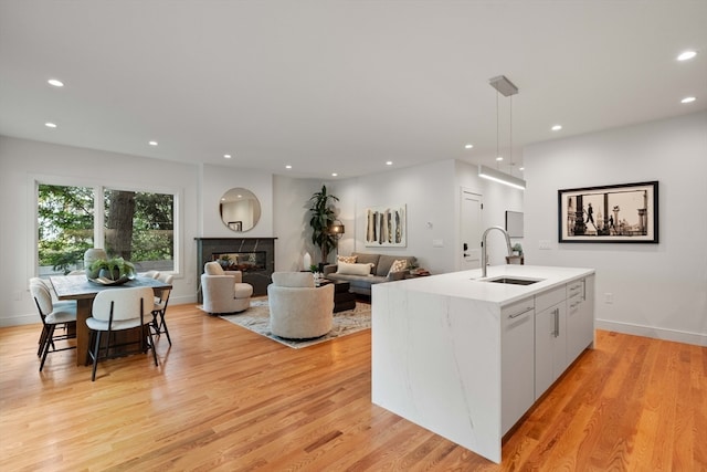 kitchen featuring light hardwood / wood-style floors, white cabinetry, an island with sink, pendant lighting, and sink