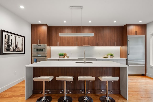 kitchen featuring light hardwood / wood-style floors, an island with sink, decorative light fixtures, and sink