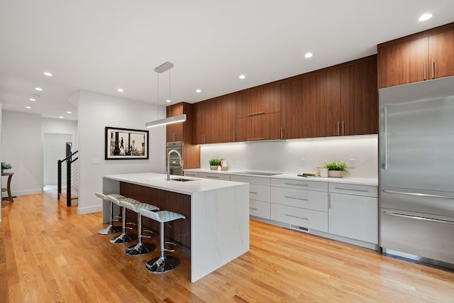 kitchen featuring hanging light fixtures, a center island with sink, stainless steel appliances, a breakfast bar area, and light hardwood / wood-style floors