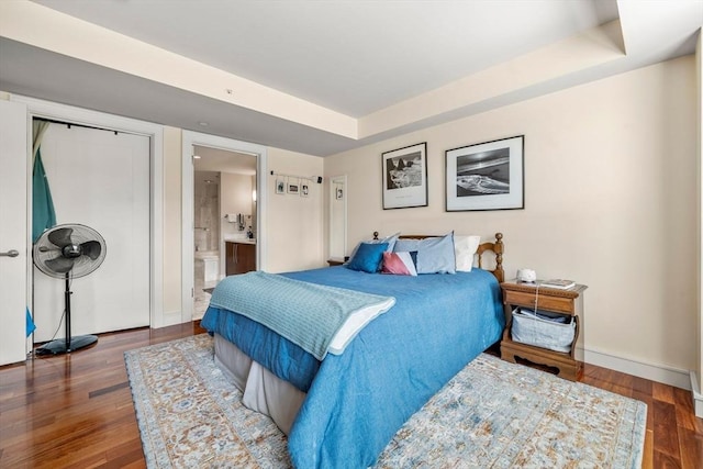 bedroom with a raised ceiling, baseboards, ensuite bathroom, and wood finished floors