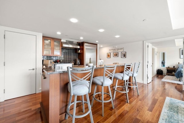 kitchen featuring light wood-type flooring, backsplash, wall chimney range hood, and glass insert cabinets