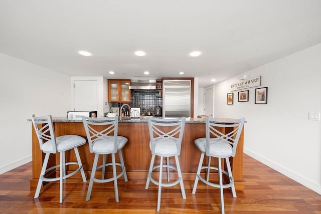 kitchen featuring light wood-type flooring, decorative backsplash, a kitchen bar, and stainless steel built in refrigerator