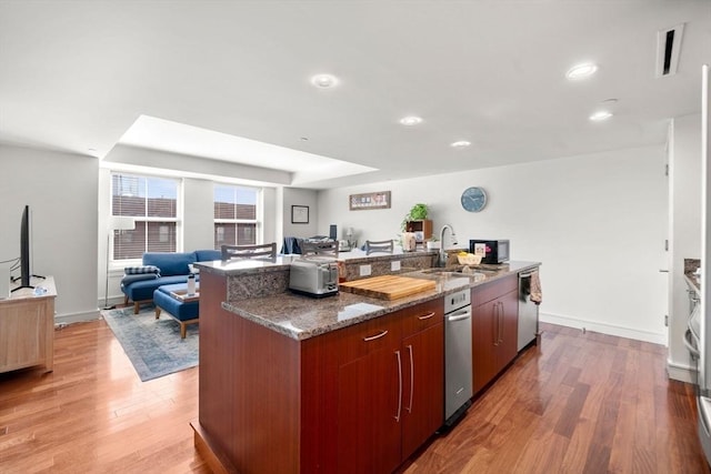 kitchen with a sink, dishwasher, light wood-style flooring, dark stone counters, and open floor plan