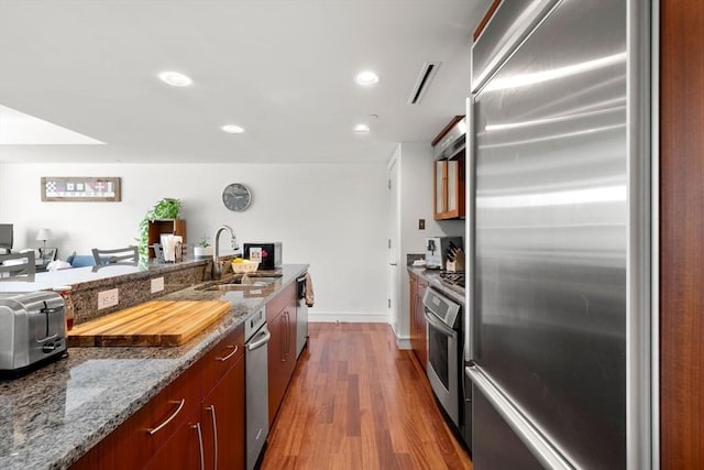 kitchen featuring wood finished floors, open floor plan, a sink, stone counters, and stainless steel appliances