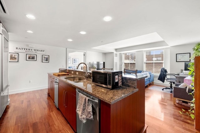 kitchen featuring stainless steel dishwasher, open floor plan, a center island with sink, a sink, and light wood finished floors