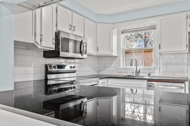 kitchen with a sink, tasteful backsplash, white cabinetry, stainless steel appliances, and dark stone counters