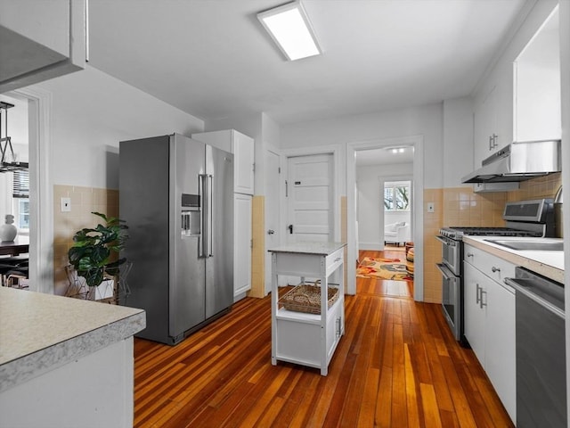 kitchen featuring dark wood-style flooring, light countertops, white cabinetry, under cabinet range hood, and appliances with stainless steel finishes