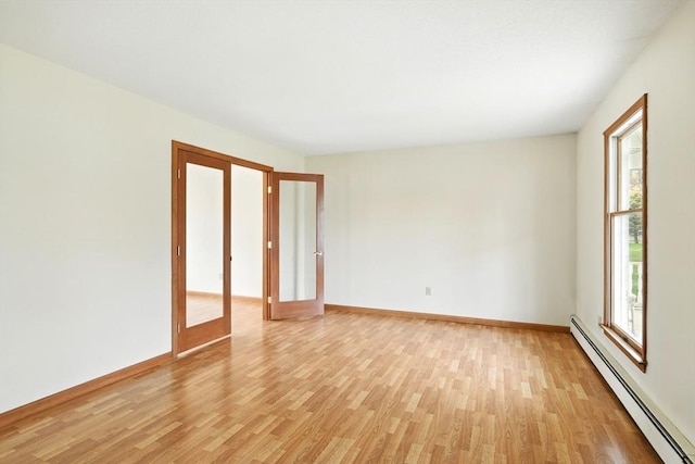 spare room with baseboards, a baseboard heating unit, and light wood-type flooring