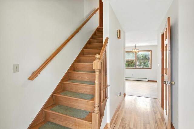 staircase with an inviting chandelier, baseboards, a baseboard radiator, and wood finished floors