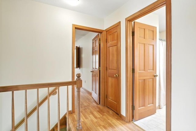corridor with baseboards, an upstairs landing, and light wood-style flooring