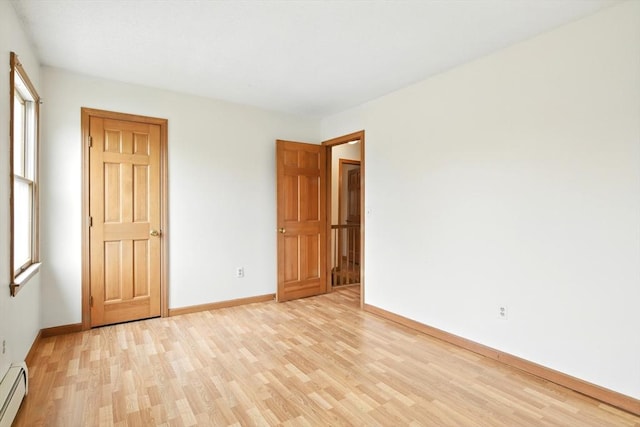 unfurnished bedroom with baseboards, a baseboard radiator, and light wood finished floors