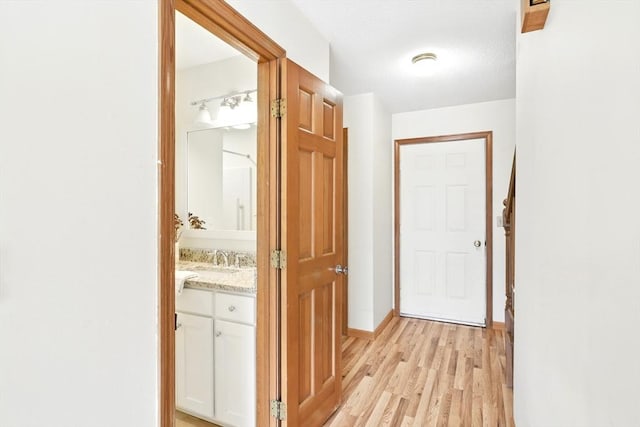 hallway featuring light wood-style floors, a sink, and baseboards