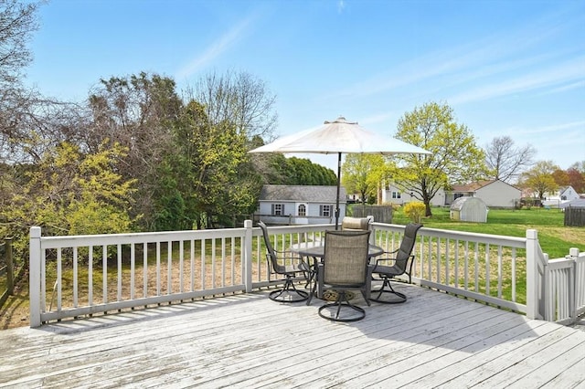 wooden terrace featuring a storage shed, an outbuilding, a lawn, and outdoor dining space
