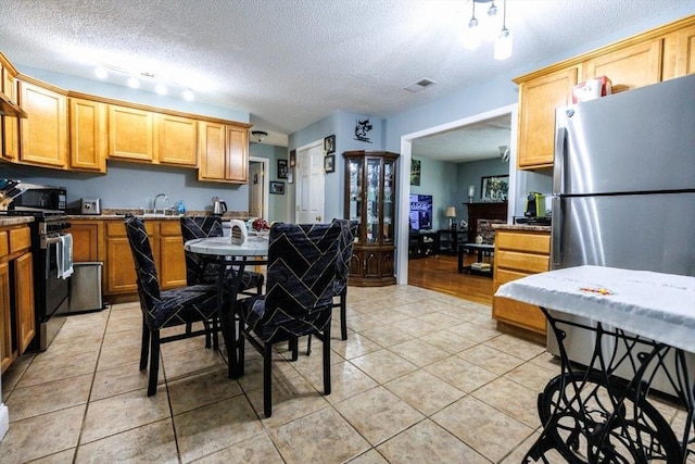 kitchen with light tile patterned floors, sink, stainless steel fridge, range, and a textured ceiling