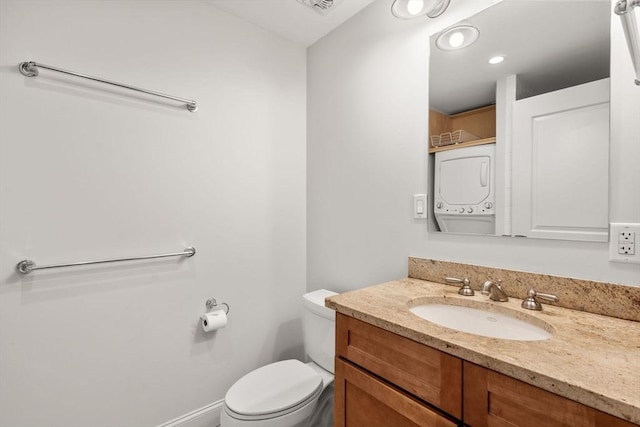 bathroom featuring stacked washing maching and dryer, vanity, and toilet