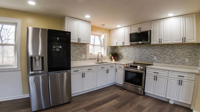 kitchen with appliances with stainless steel finishes, dark wood-type flooring, sink, pendant lighting, and white cabinets