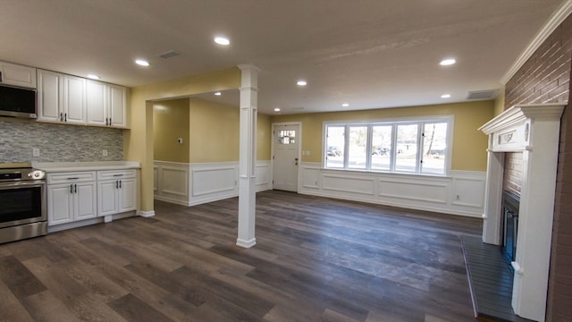 kitchen with white cabinetry, a brick fireplace, dark hardwood / wood-style flooring, decorative backsplash, and appliances with stainless steel finishes