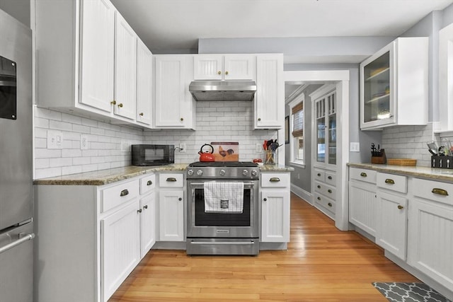 kitchen with tasteful backsplash, appliances with stainless steel finishes, white cabinets, light wood-type flooring, and under cabinet range hood