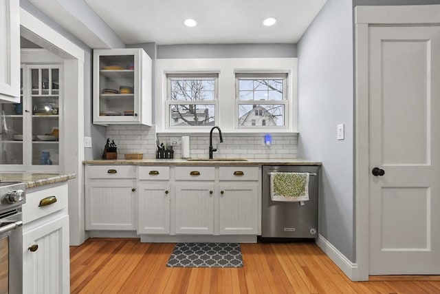 bar featuring stove, a sink, decorative backsplash, dishwasher, and light wood finished floors