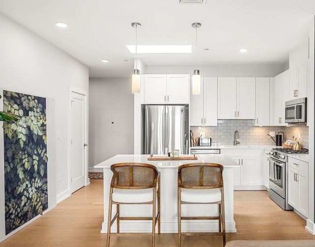 kitchen featuring appliances with stainless steel finishes, light wood-type flooring, white cabinetry, and pendant lighting