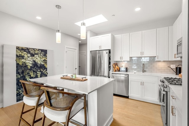 kitchen with white cabinets, stainless steel appliances, light hardwood / wood-style flooring, and a kitchen island