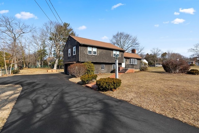 view of home's exterior with an attached garage, a lawn, driveway, and a chimney