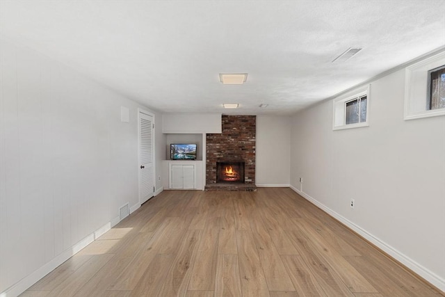 unfurnished living room featuring visible vents, a textured ceiling, a fireplace, light wood finished floors, and baseboards