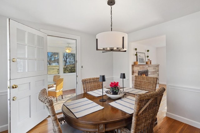 dining area with baseboards, a stone fireplace, and wood finished floors