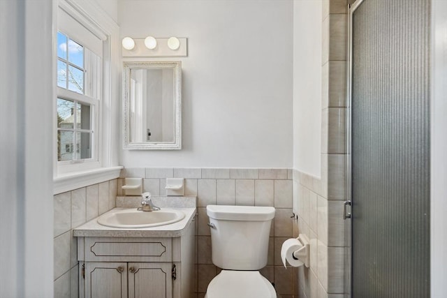 bathroom with an enclosed shower, toilet, tile walls, wainscoting, and vanity