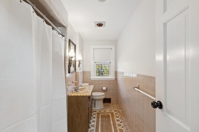 bathroom with vanity, a wainscoted wall, tile patterned flooring, tile walls, and toilet