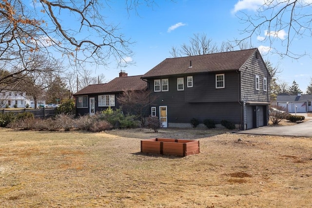 back of house with roof with shingles, driveway, an attached garage, a yard, and a chimney