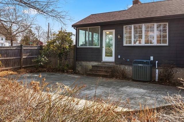 exterior space featuring cooling unit, fence, roof with shingles, and a patio area