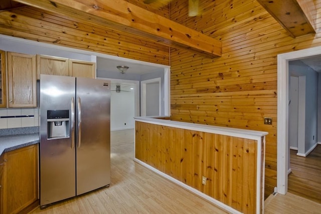 kitchen featuring beamed ceiling, stainless steel fridge, light hardwood / wood-style flooring, and wood walls