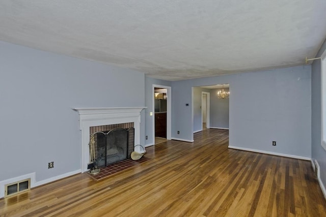 unfurnished living room featuring a brick fireplace, dark hardwood / wood-style floors, and a chandelier