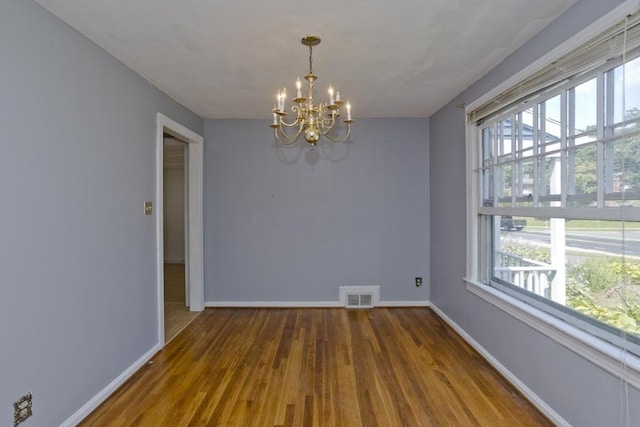 unfurnished room featuring a healthy amount of sunlight, hardwood / wood-style floors, and a notable chandelier