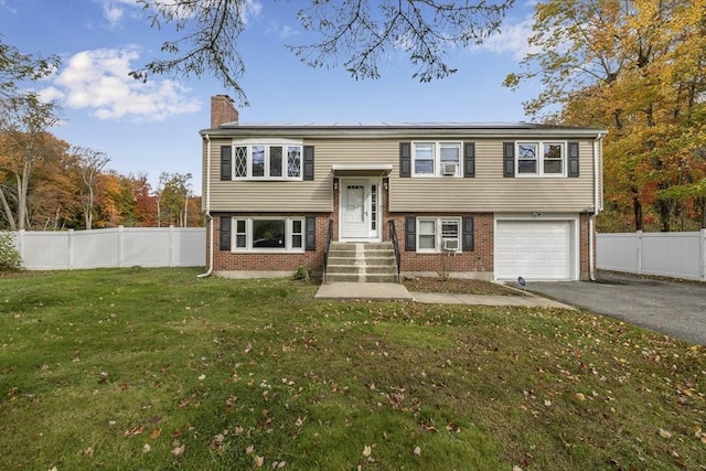 split foyer home featuring aphalt driveway, fence, roof mounted solar panels, a front lawn, and a chimney