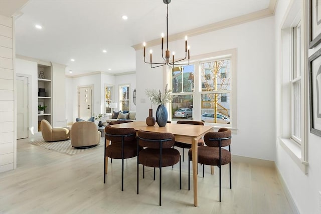 dining space featuring ornamental molding, light hardwood / wood-style floors, built in features, and an inviting chandelier