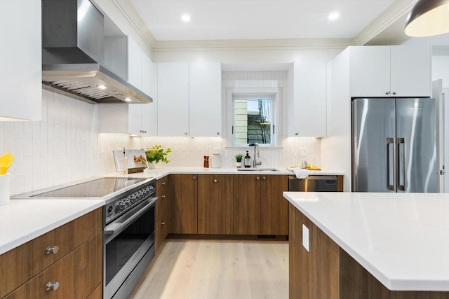 kitchen featuring white cabinets, crown molding, wall chimney exhaust hood, light hardwood / wood-style floors, and stainless steel appliances