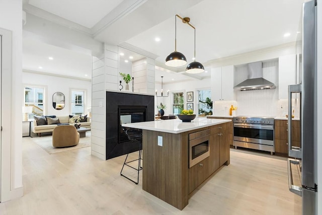 kitchen featuring a center island, wall chimney exhaust hood, light hardwood / wood-style floors, white cabinetry, and stainless steel appliances