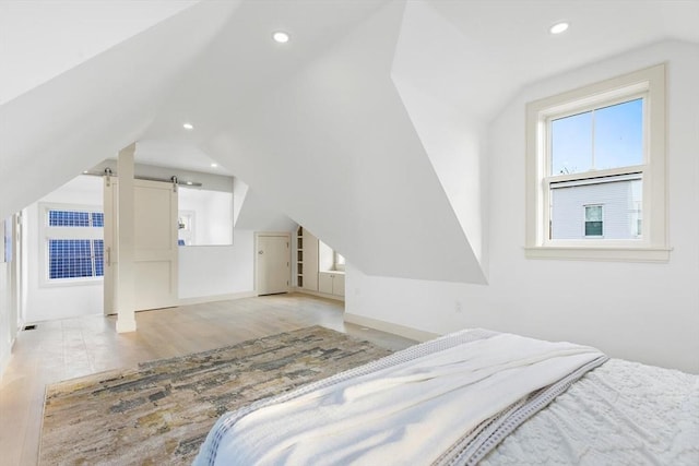 bedroom featuring a barn door, light hardwood / wood-style floors, and vaulted ceiling