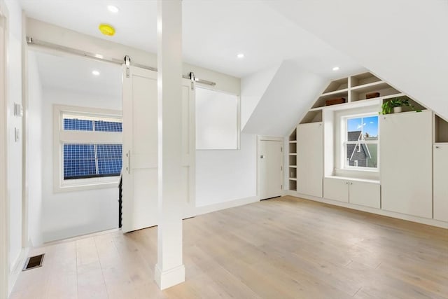 bonus room with a barn door and light hardwood / wood-style floors