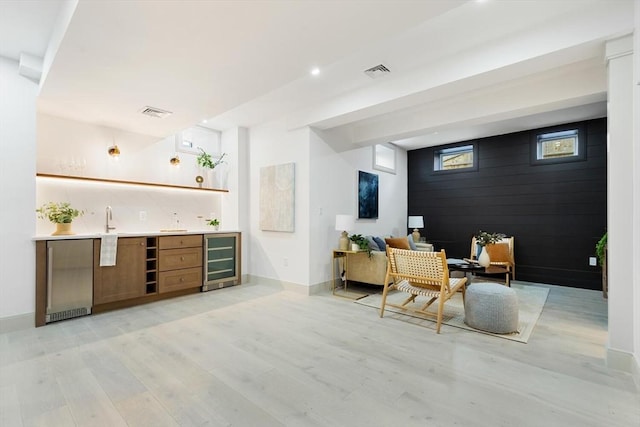 bar featuring stainless steel fridge, sink, beverage cooler, and light hardwood / wood-style floors