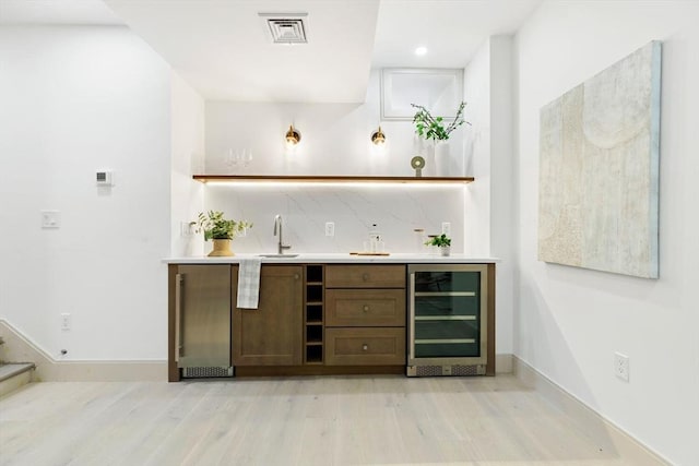 bar with wine cooler, decorative backsplash, light hardwood / wood-style flooring, and sink