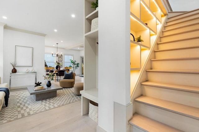 stairway with hardwood / wood-style flooring, crown molding, and an inviting chandelier